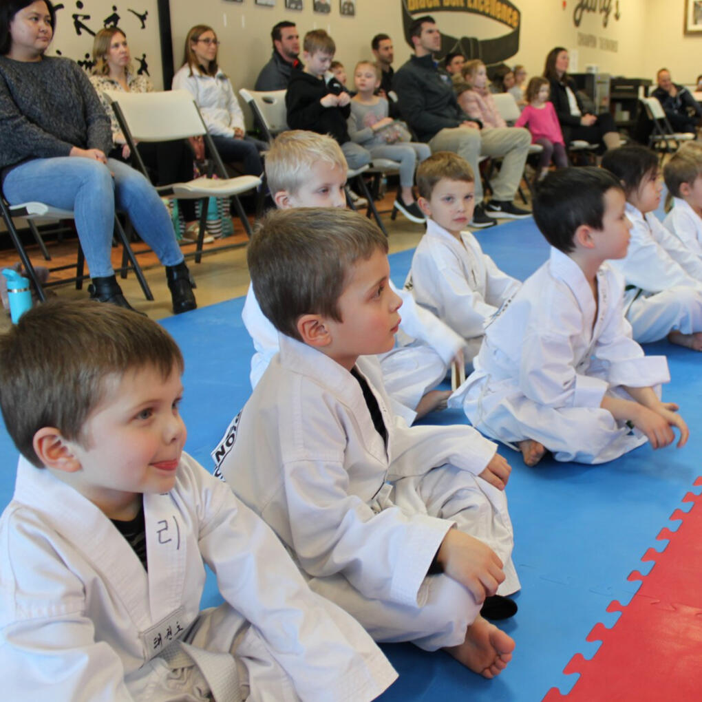 A group of 3-4 year old students sitting crisscross demonstrating patience and focus