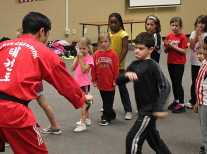 Master Jung is holding a kicking target for a child in a class at the public library